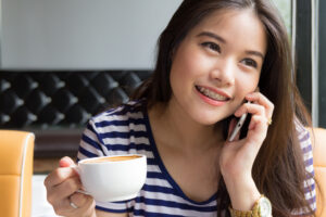 A woman talks on the phone and drinks coffee while wearing braces