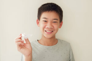 Smiling child holding a clear Invisalign aligner